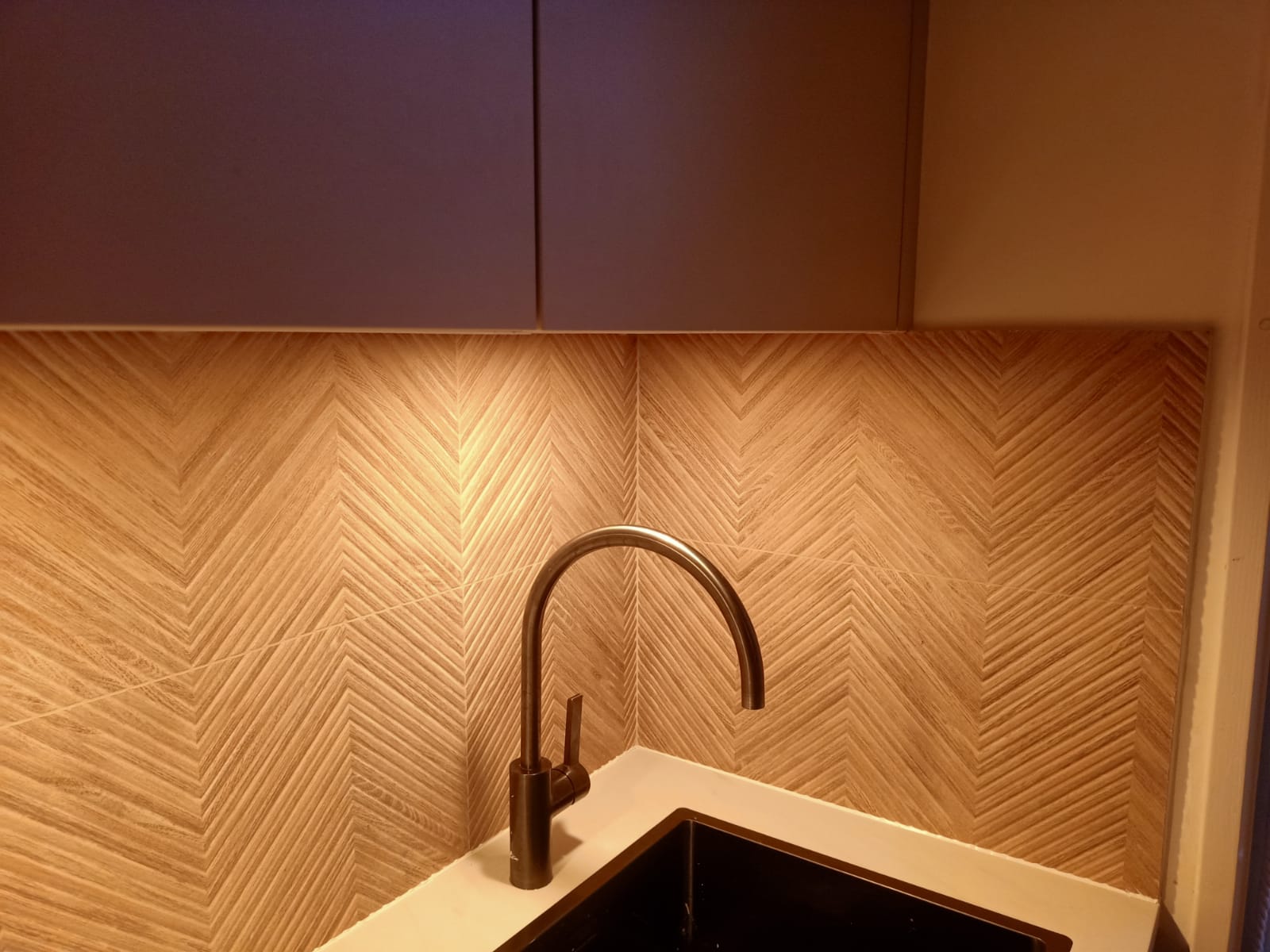 Achterwand met visgraattegels in houtlook achter een hoekspoelbak met zwarte kraan