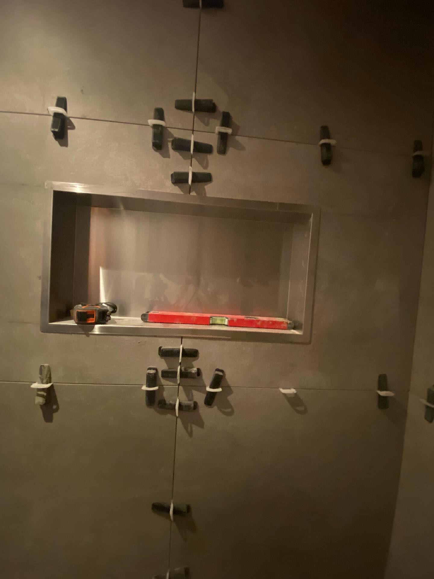 Donker betegelde douchewand met ingebouwde rvs-nis en een waterpas